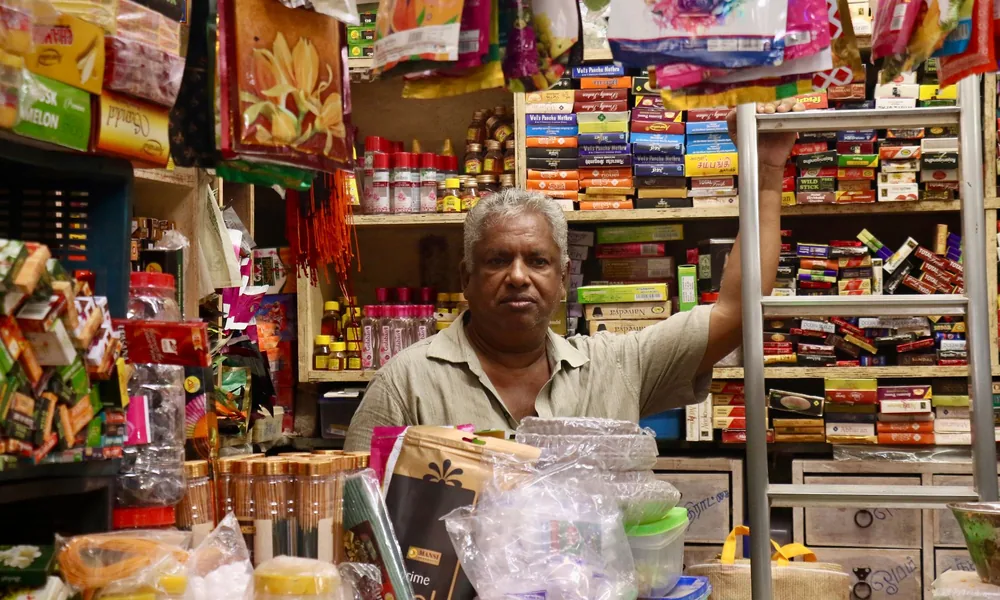 Kiryana store shopkeeper behind a stocked counter, using grocery store software